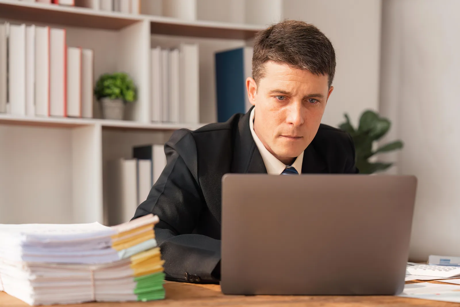 Personal injury lawyer working on a laptop next to a stack of case files, reviewing AI-assembled records