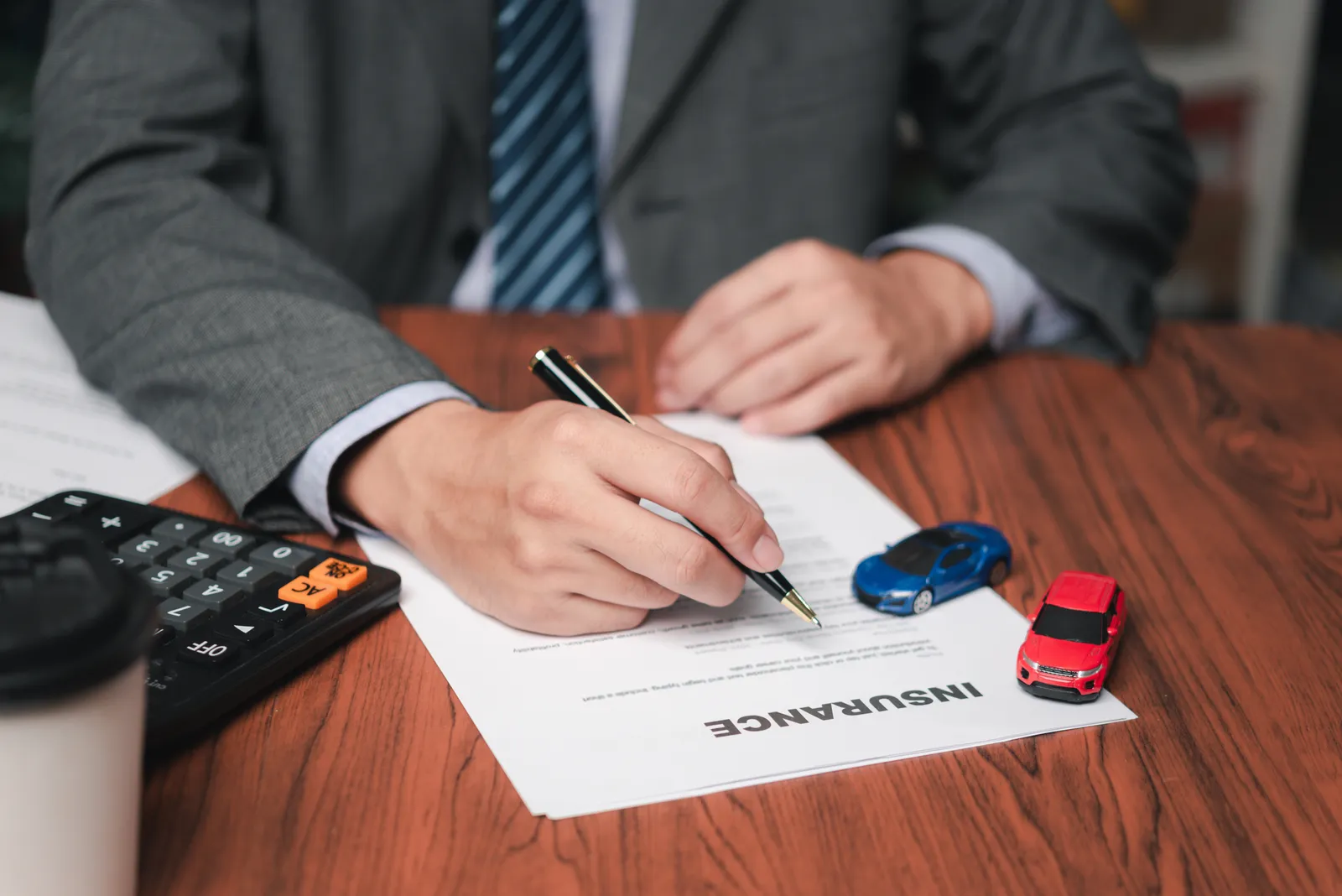 Person signing auto insurance documents at a desk, illustrating a California time-limited policy limits demand