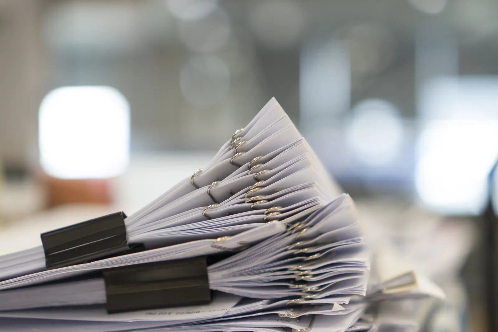 Stack of old paper records held with binder clips on an office desk